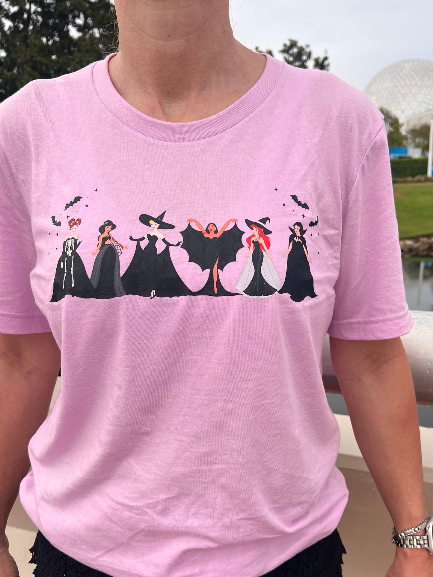 Light lilac T-shirt featuring six princess silhouettes dressed in black gothic Halloween costumes, with bats flying above them.