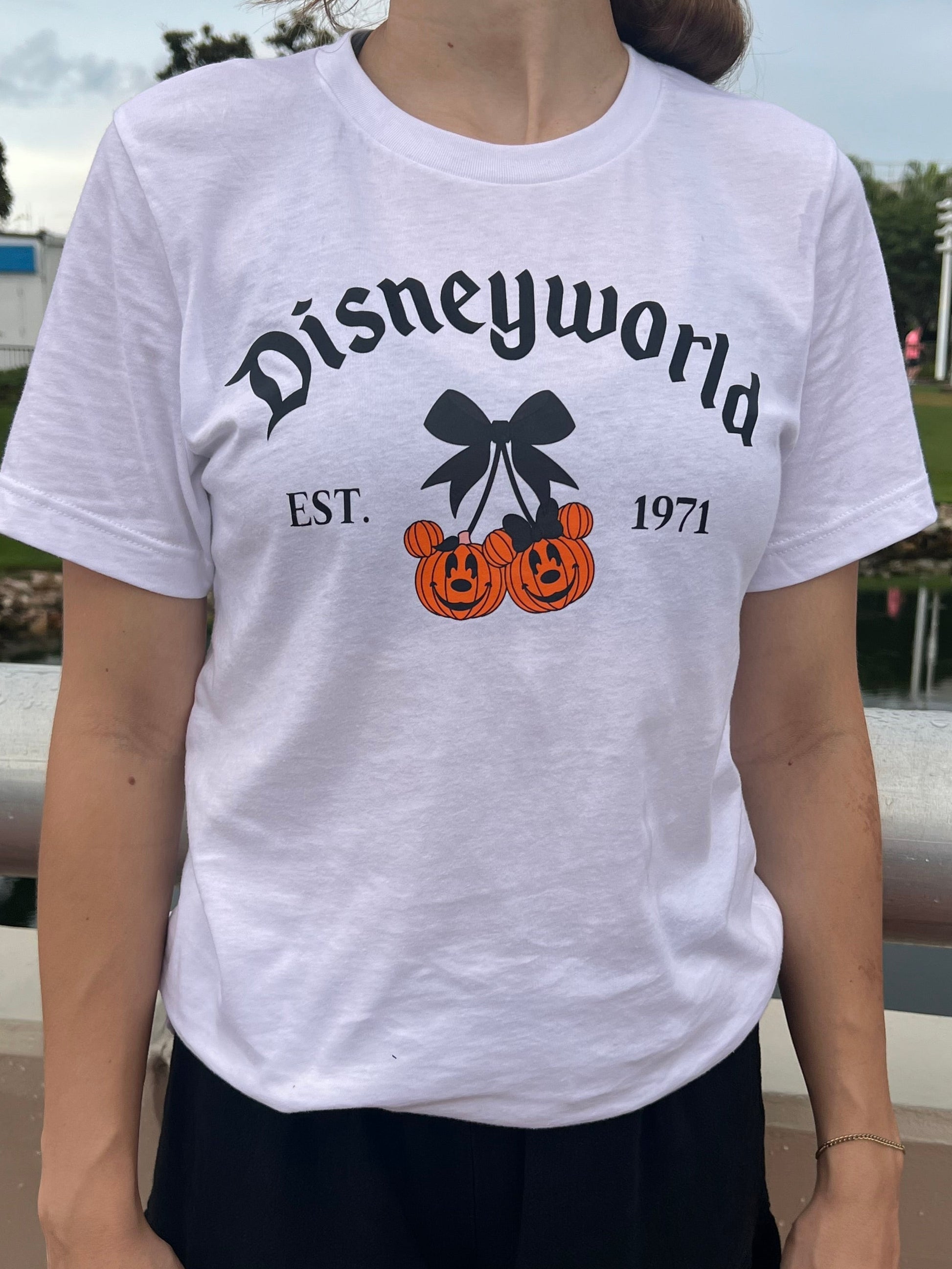 White unisex T-shirt with the word “Disneyworld” in gothic lettering and two Mickey pumpkin heads tied with a black bow, styled with “EST. 1971.”