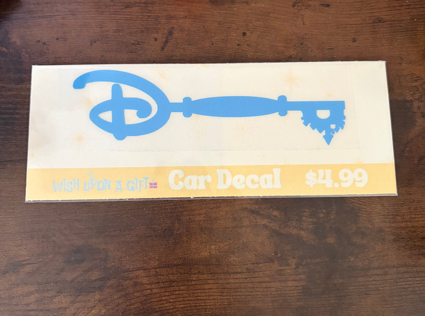 Car decal packaging with graphics of disney key and text on a wooden surface